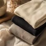 Minimal editorial lifestyle composition featuring soft bamboo comfort crew socks in ivory, black, and beige tones arranged on linen fabric with warm natural lighting.